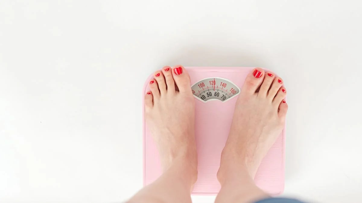 Top view of crop anonymous barefoot female measuring weight on scales on white background